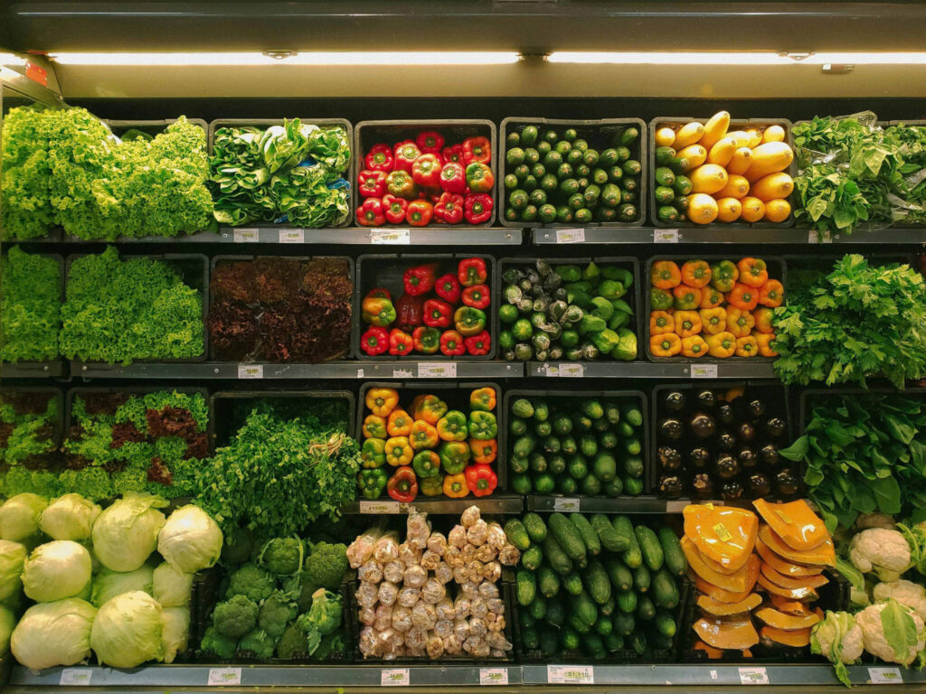 Refrigerated supermarket shelves stocked with fresh green vegetables and peppers